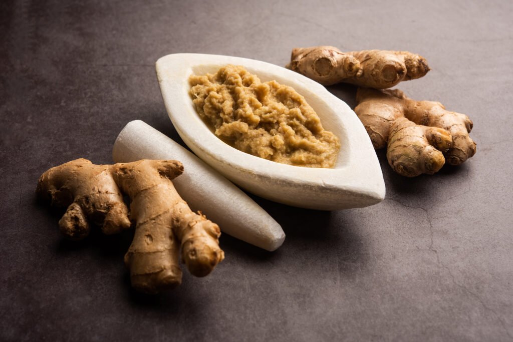 fresh mashed ginger paste or puree in a bowl and whole adrak over moody background, selective focus